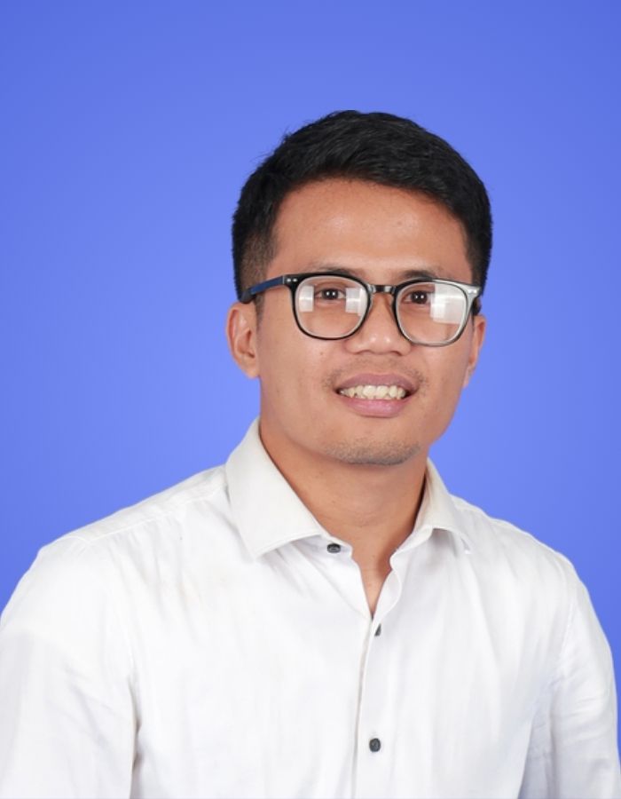 Professional headshot of Handoko from the SitesGuru website and design support team, wearing a white shirt and glasses with a blue background.